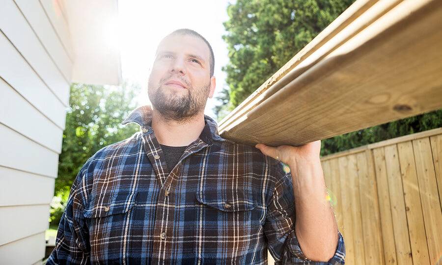 Ein Mann trägt Holzlatten auf der Schulter und die Sonne scheint