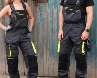 zwei Personen tragen schwarze Arbeitslatzhose mit gelben Elementen, Hintergrund eine Holzwand